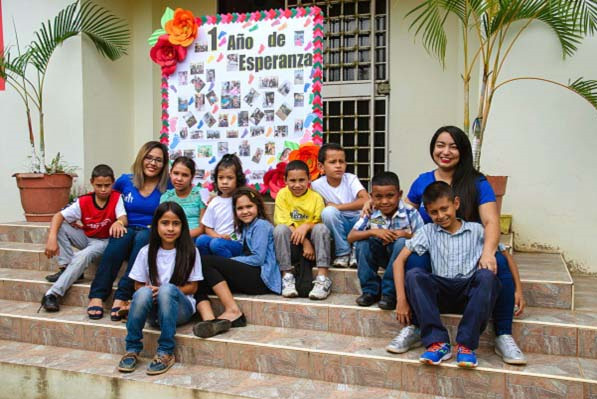 The growing Casa Mi Esperanza family sits together on the steps of their home.